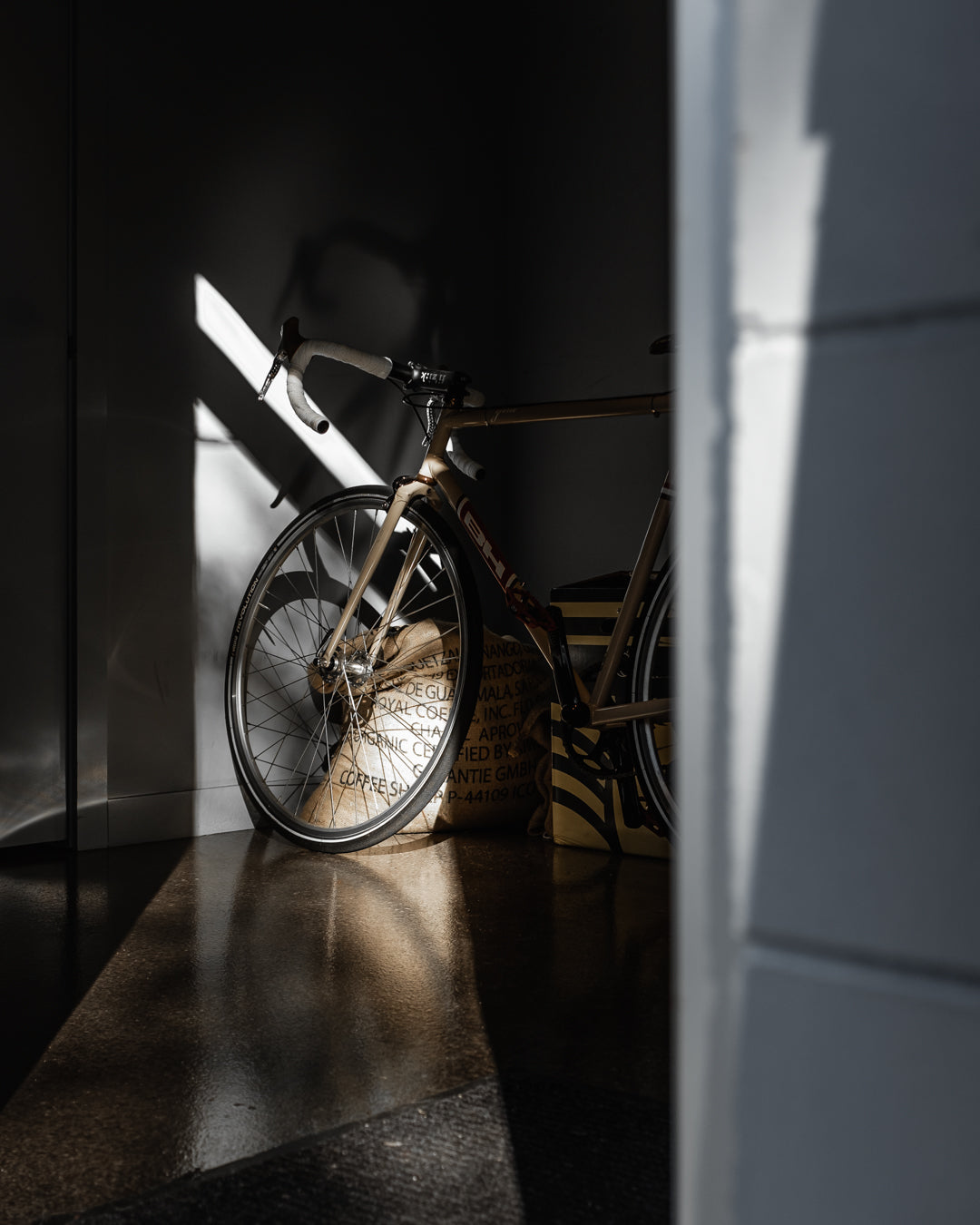 Road bike leaning against the wall inside The Roasted Record beside burlap coffee sacks